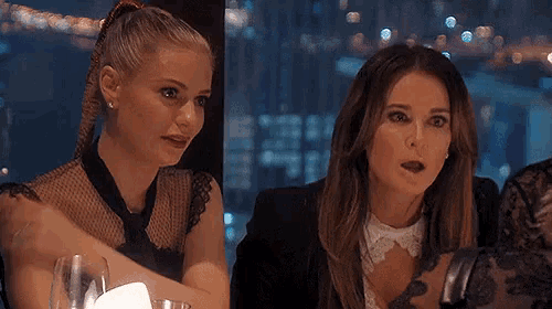 two women are sitting at a table with their mouths open