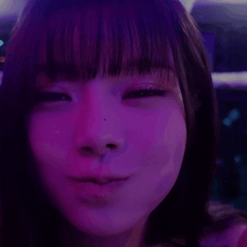 a close up of a woman 's face with purple lighting behind her