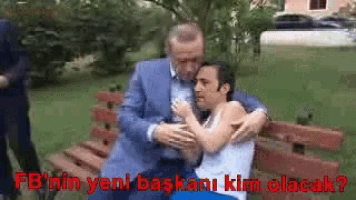 a man in a suit is hugging another man while sitting on a park bench .