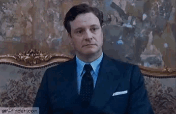 a man in a suit and tie is sitting in front of a painting .