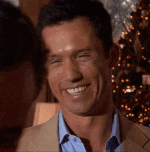 a man in a suit and blue shirt smiles with a christmas tree in the background