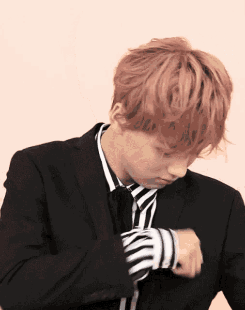 a young man with pink hair is wearing a black suit and tie