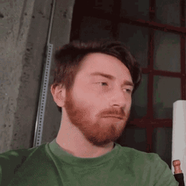 a man with a beard is wearing a green shirt and looking at the camera
