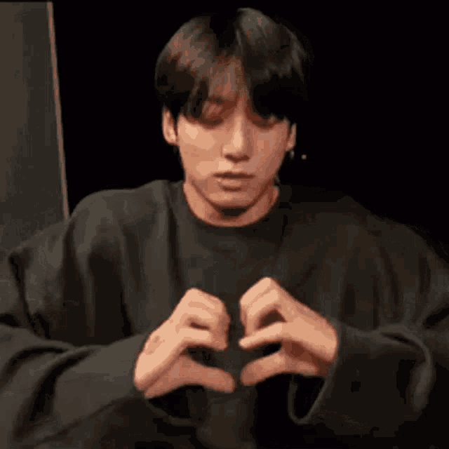 a young man in a black shirt is making a heart shape with his hands .