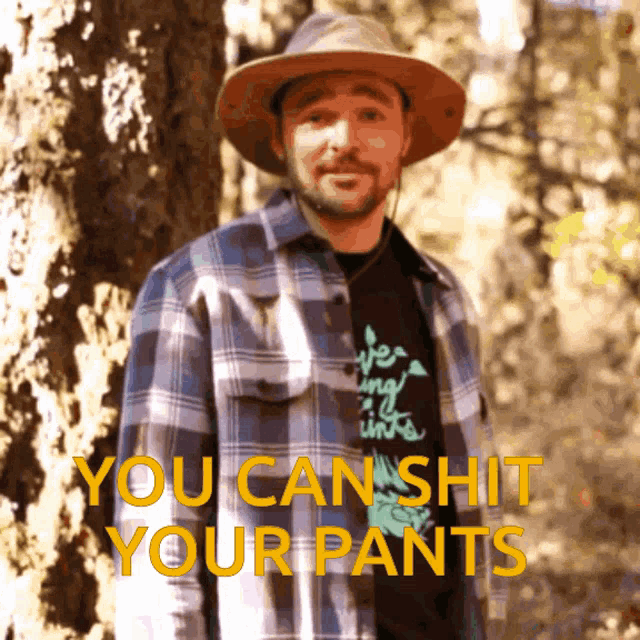 a man wearing a plaid shirt and a hat with the words you can shit your pants on the bottom