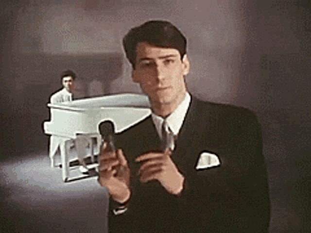 a man in a suit and tie is holding a microphone in front of a piano