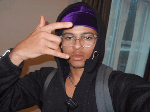 a man wearing a black hoodie and a purple headband is making a peace sign