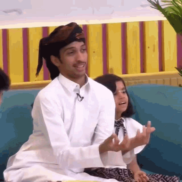 a man and a little girl are sitting on a couch and the man is wearing a turban