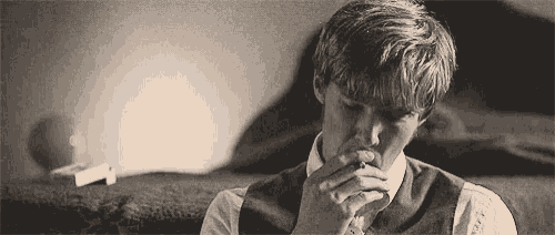 a man is smoking a cigarette while sitting on a bed in a black and white photo .