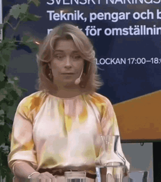 a woman wearing a microphone stands in front of a sign that says lockan 17 00 18 3