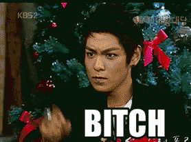 a man is standing in front of a christmas tree with the word bitch on his face