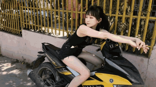 a woman sits on a yellow and black yamaha scooter
