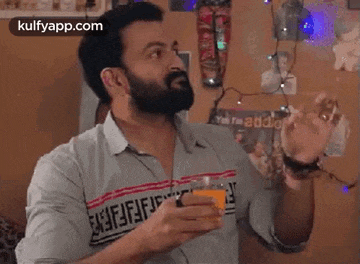 a man with a beard is holding a glass of orange juice in his hand .