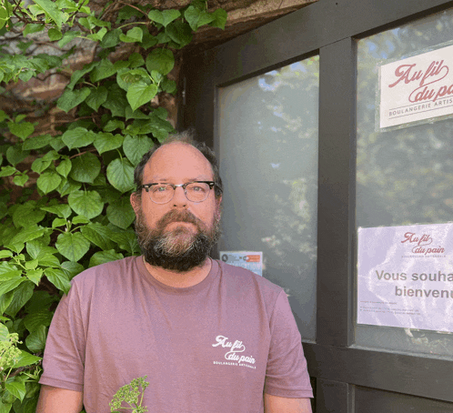 a man wearing a shirt that says au fil du pain stands in front of a door