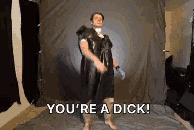 a man in a black robe is standing in front of a black curtain and says you 're a dick