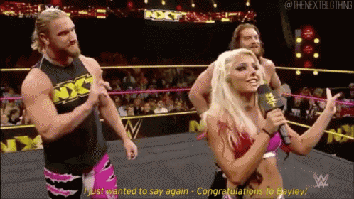 a woman is holding a microphone in a wrestling ring while a man and woman stand behind her