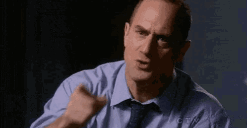 a man in a blue shirt and tie is sitting in a dark room .