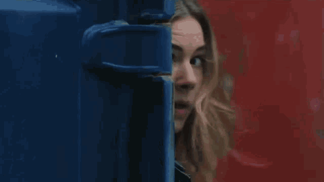 a woman peeking out from behind a blue container