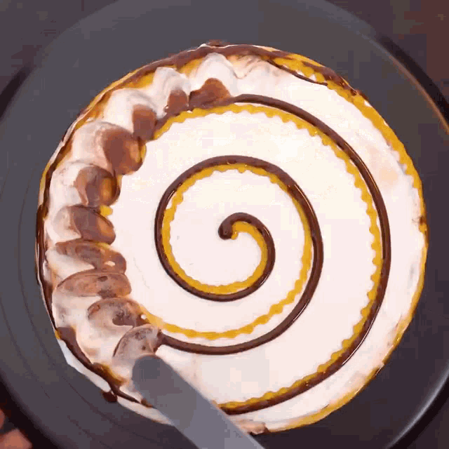 a cake with a chocolate swirl on it is being cut with a knife