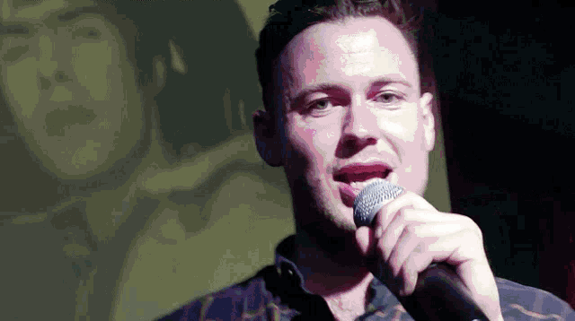 a man singing into a microphone with a blurred image of a man behind him
