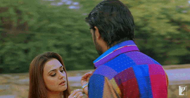 a man in a colorful shirt is putting a bracelet on a woman 's finger