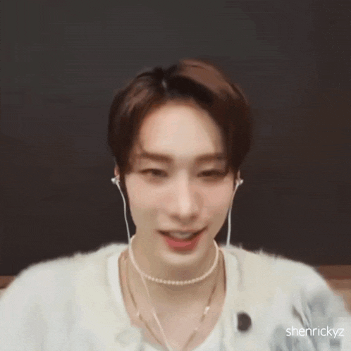 a young man wearing headphones and a pearl necklace is smiling and waving .
