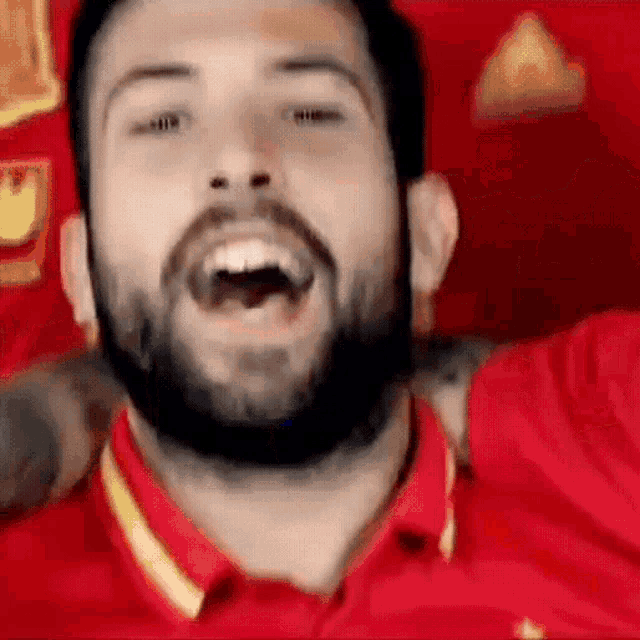 a man with a beard wearing a red shirt is laughing with his mouth open