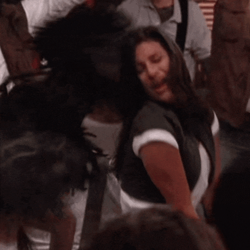 a woman is dancing in a crowd of people and smiling .