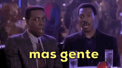 two men are sitting at a table with the words mas gente written in yellow