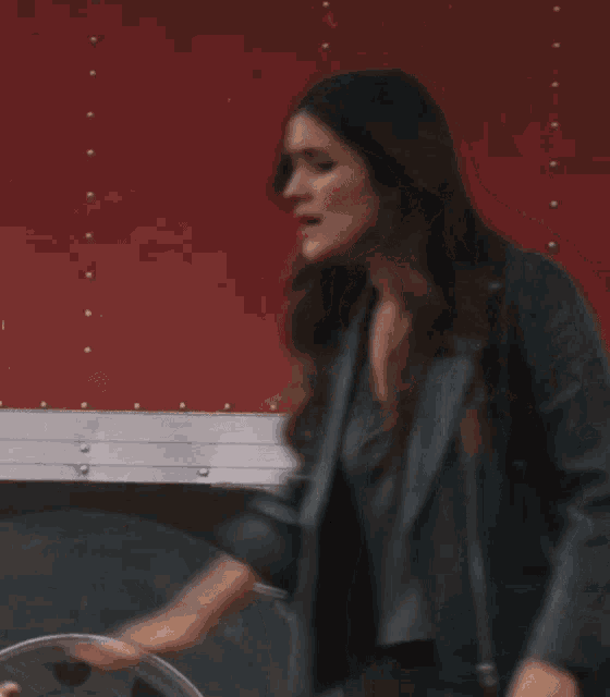 a woman wearing a black hat and a leather jacket stands in front of a red wall