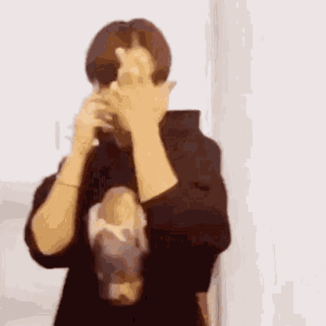 a man is covering his face with his hands while wearing a black hoodie .