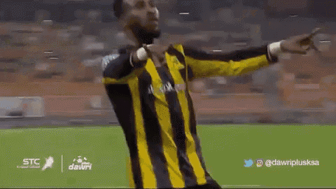a man in a yellow and black striped shirt is dancing on a soccer field ..