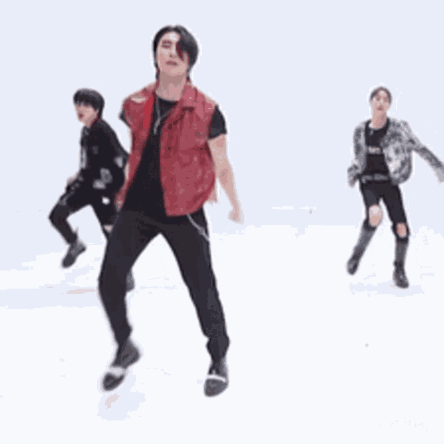 a man in a red vest is dancing with two other men in black pants .