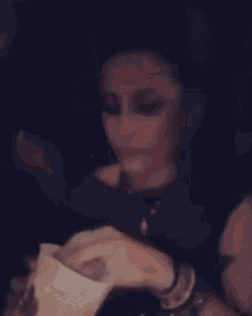 a woman is sitting at a table with a drink in her hand and eating a sandwich .