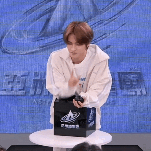 a young man is standing in front of a table holding a black box with chinese writing on it .
