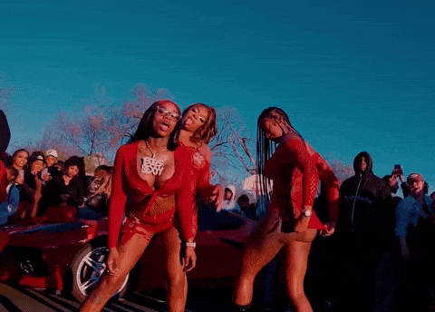 a group of women are dancing in front of a crowd and one of them has a necklace that says i love you