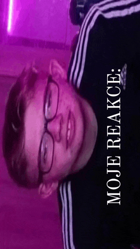 a young man wearing glasses and a black adidas shirt is standing in front of a purple wall .