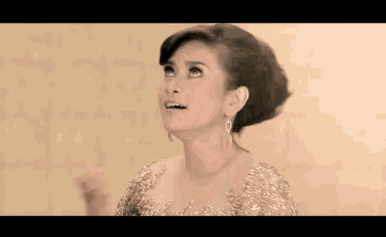 a woman in a gold dress and earrings is looking up at the sky .