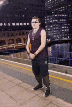 a man wearing sunglasses and a purple tank top is standing on a sidewalk