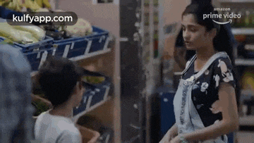 a woman and a child are standing in a grocery store talking to each other .