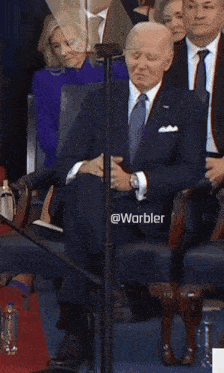 a man in a suit and tie is sitting in a chair with the words @warbler on the bottom