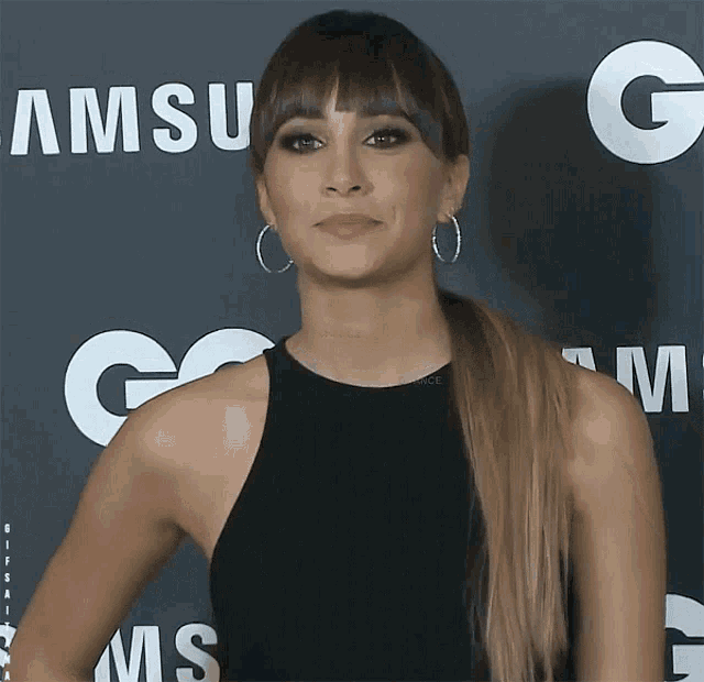 a woman wearing hoop earrings is standing in front of a samsung logo