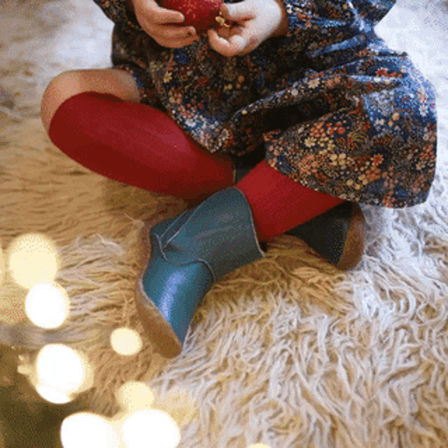 a little girl wearing red knee high socks and blue boots sits on the floor