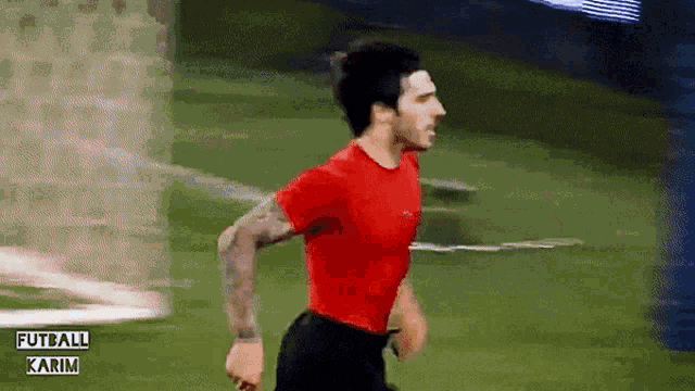 a man in a red shirt and black shorts is running on a soccer field ..