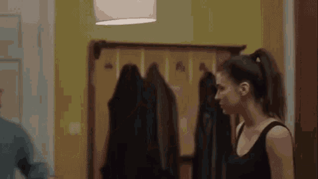 a woman in a black tank top is standing in a hallway next to a man .
