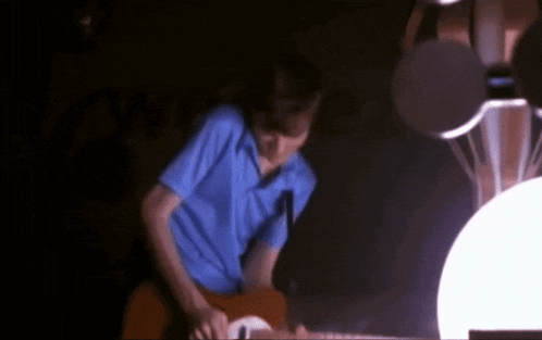 a man in a blue shirt plays a guitar in a dark room