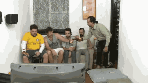 a group of men are sitting on a couch watching a television