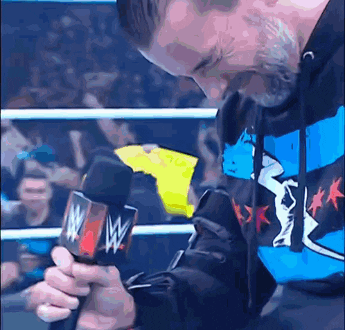 a man in a wrestling ring holds a microphone with the letter w on it