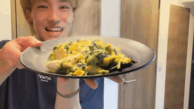 a man is holding a plate of food with a t-shirt that says essential on it