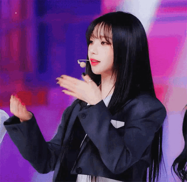 a woman with long black hair is wearing a blazer and a microphone